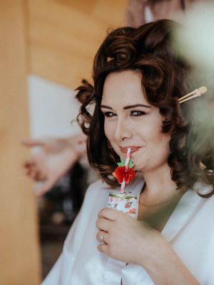 Braut lacht mit Getränk in die Kamera bei Fertigmachen