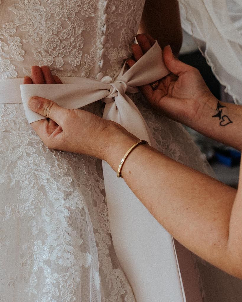 Detailfoto Person bindet Schleife beim Hochzeitskleid